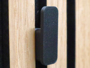 Minimalist black wall hook securely attached to acoustic panels, offering a modern and sleek design for hanging coats and accessories.