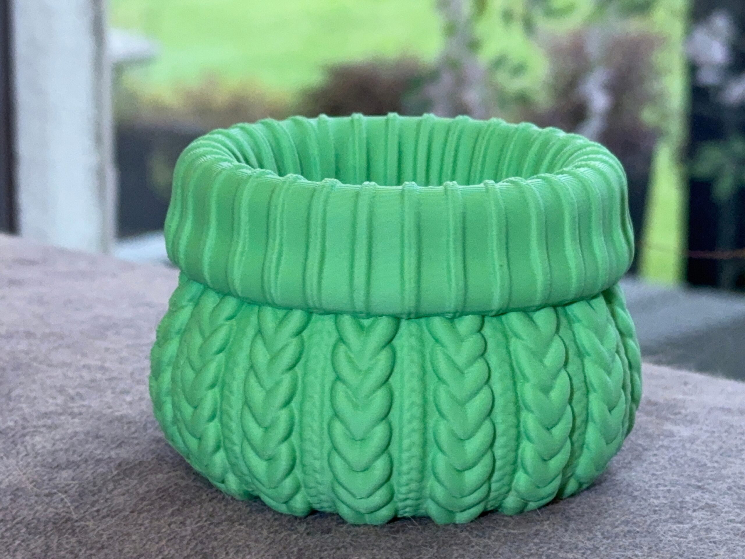 Green cable knit planter with a rounded base and chunky ribbed rim.