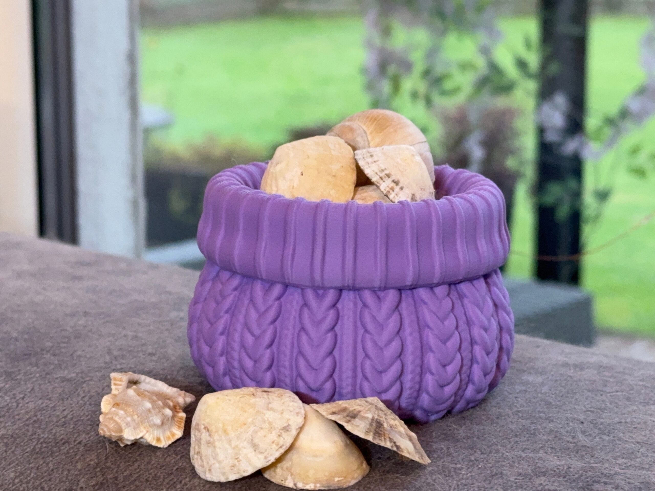 Purple cable knit pot holding seashells, with more shells arranged in front.